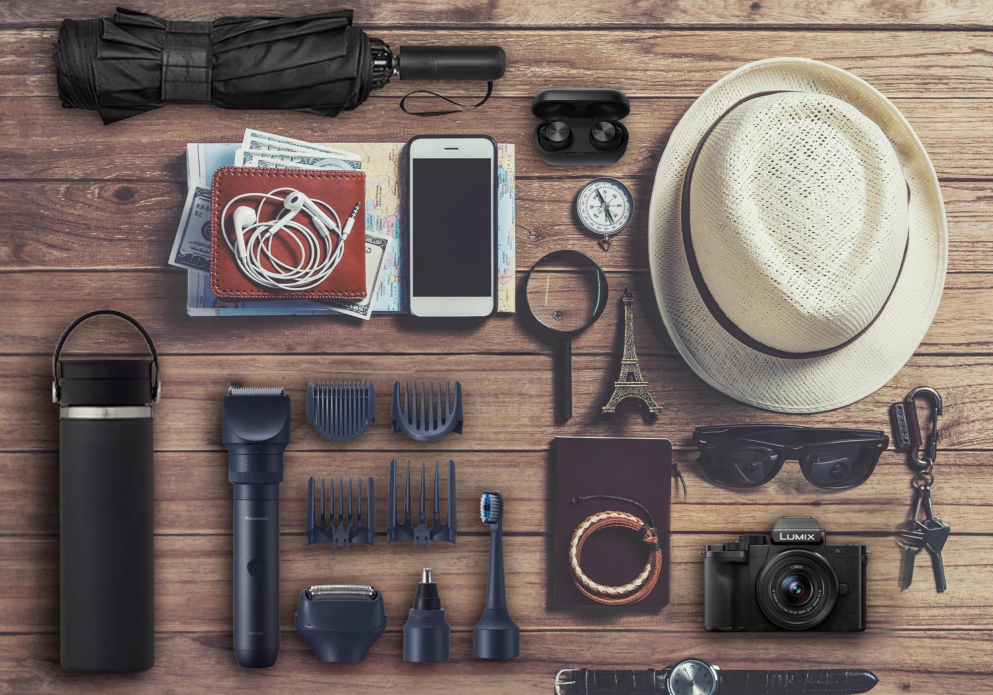 Travel-ready collection of Panasonic gear on a wooden surface, including a Lumix camera, noise-canceling earbuds, smartphone, and grooming kit