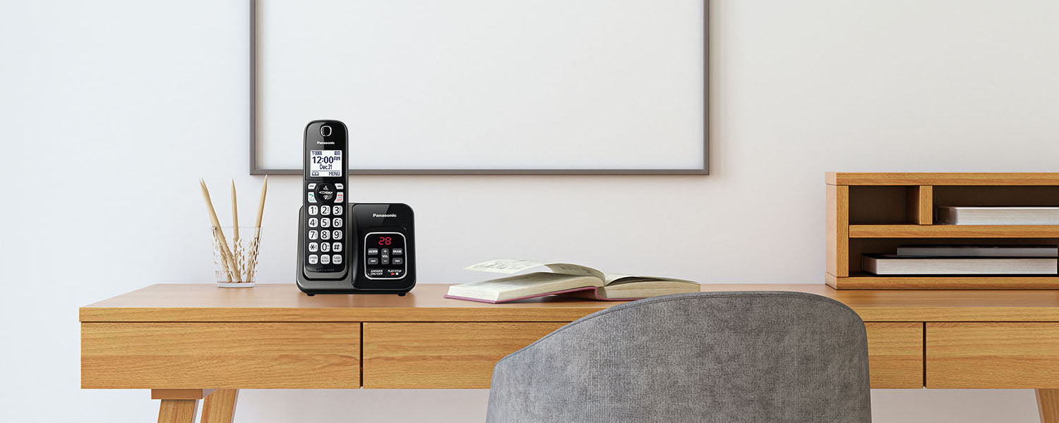 A cordless phone sits on top of a wooden desk