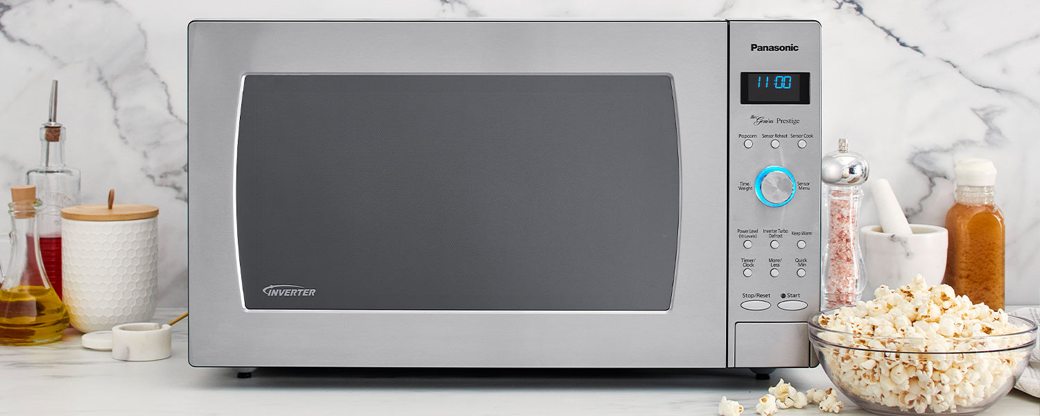 A microwave oven sits on top of a kitchen countertop with a bowl of popcorn next to it and various spices in the background