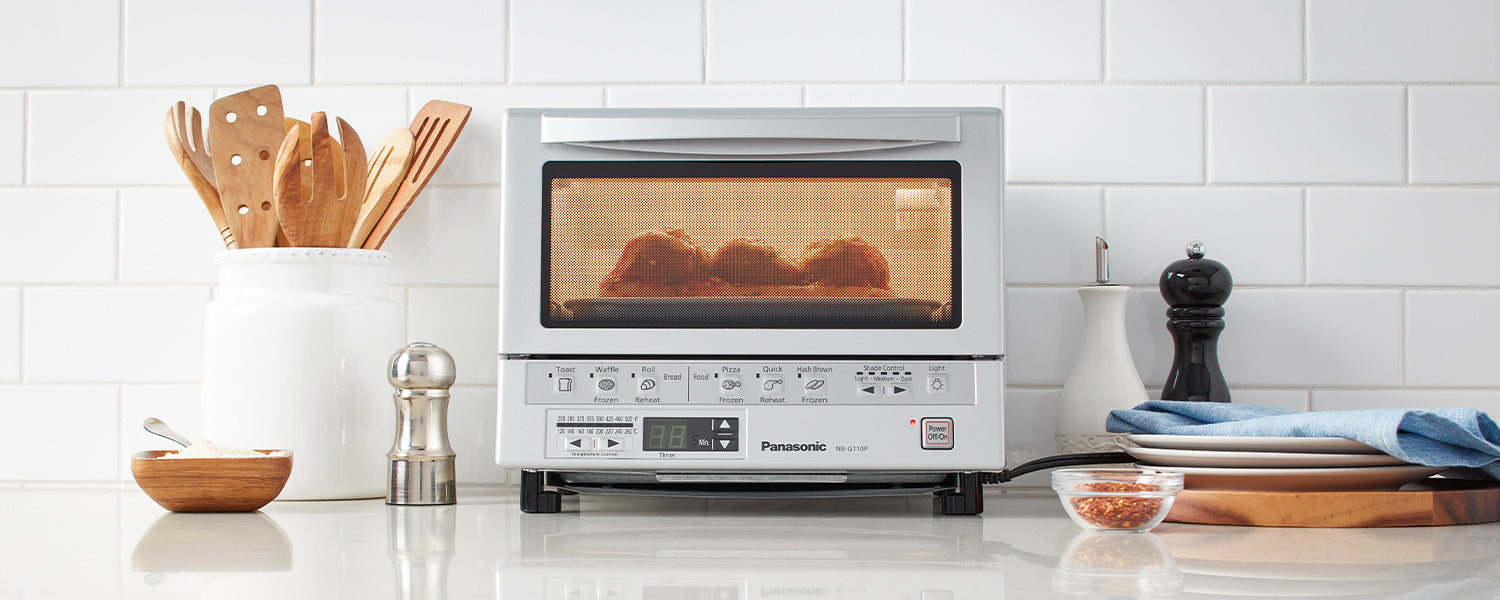 A toaster oven with food inside it on top of a kitchen counter with various kitchen utensils and spices
