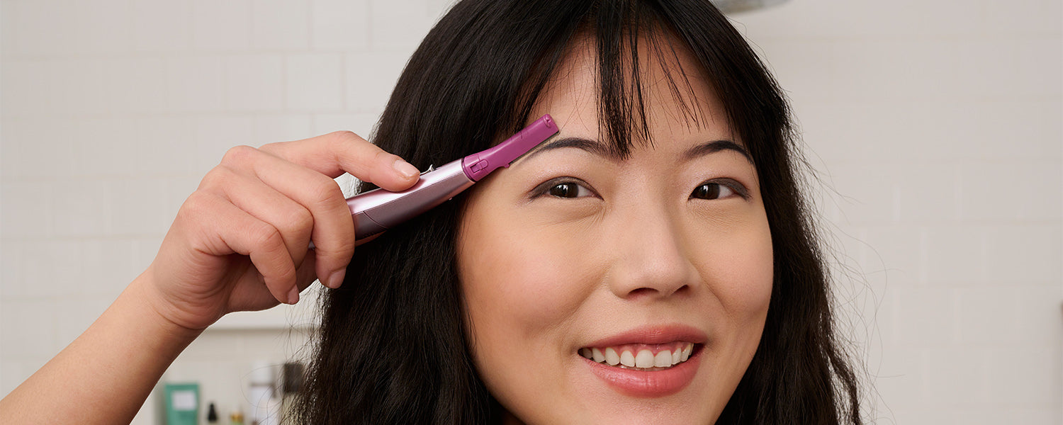 woman using a facial hair trimmer to shape her eyebrows