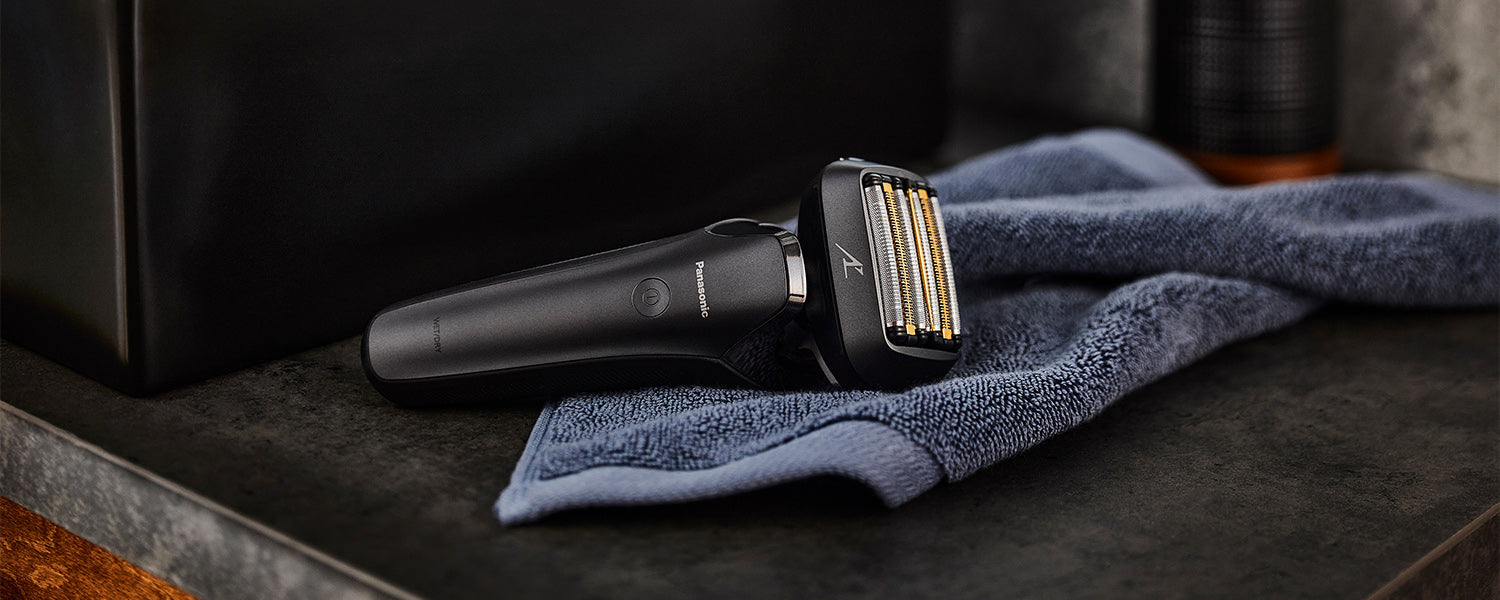 A Panasonic men's electric shaver sits on top of a blue towel set on a dark bathroom vanity