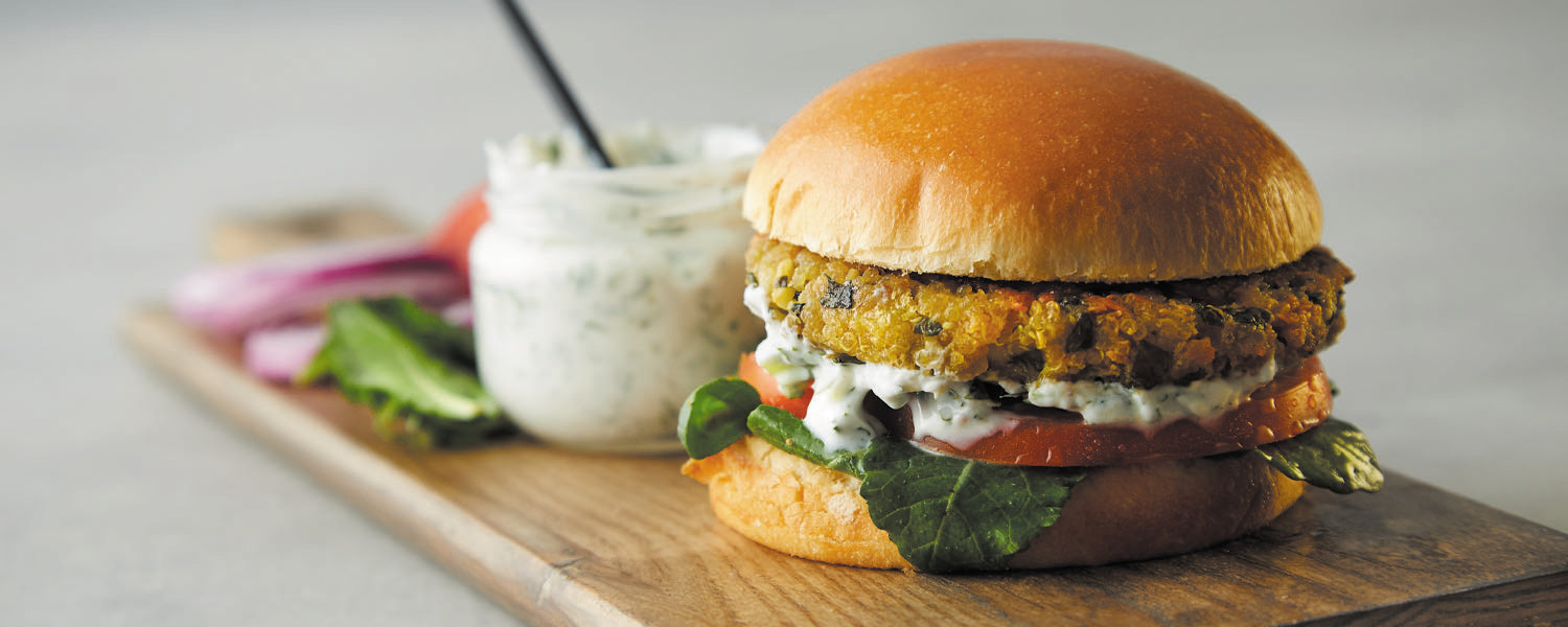Mediterranean Kale Quinoa burger with bun sits on top of wooden serving plank