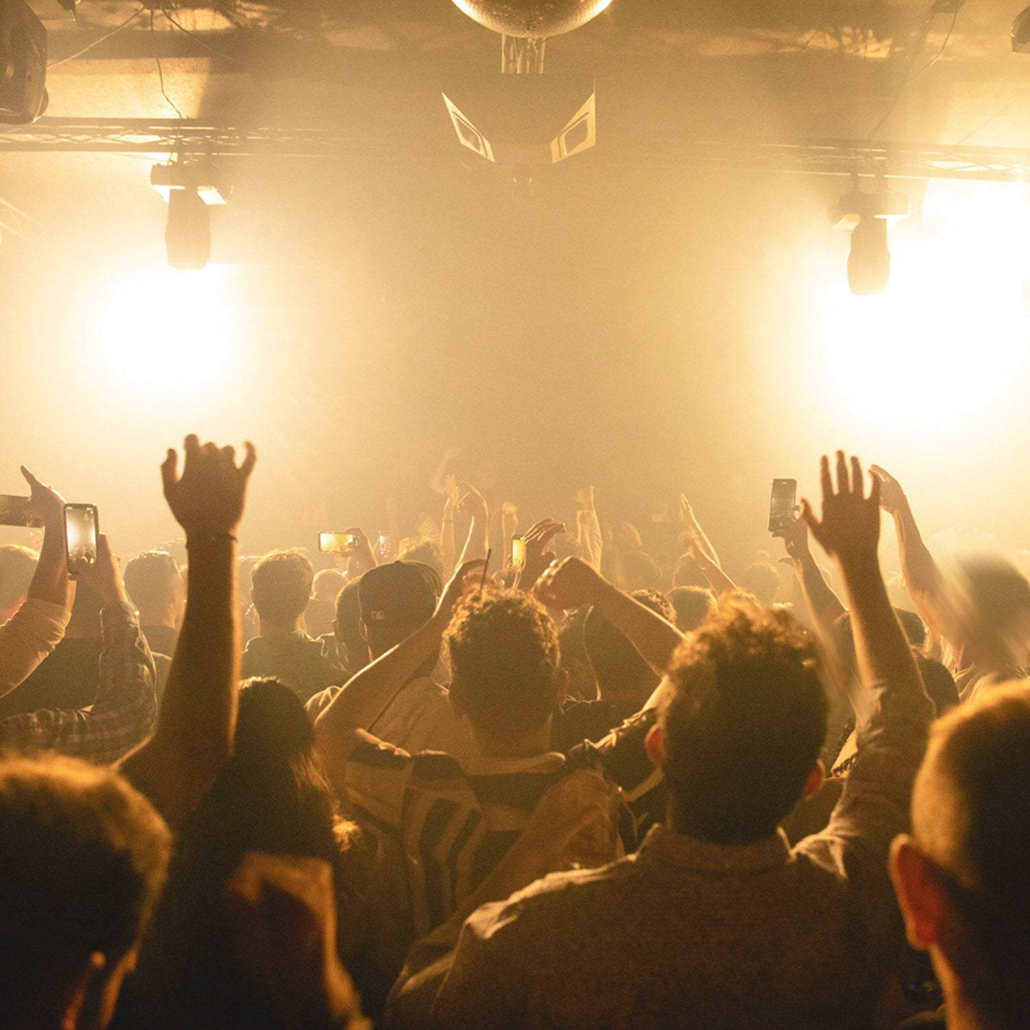 People at a concert with raised hands and stage lights.