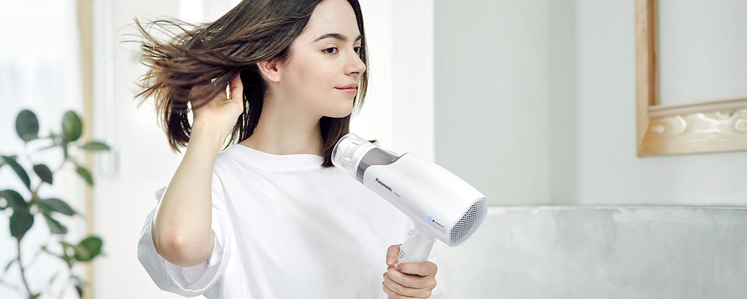 woman stands in a bright room of the home and uses a white hair dryer