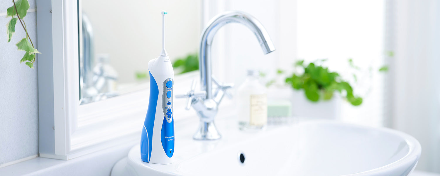 An oral irrigator sits on the edge of a bathroom sink