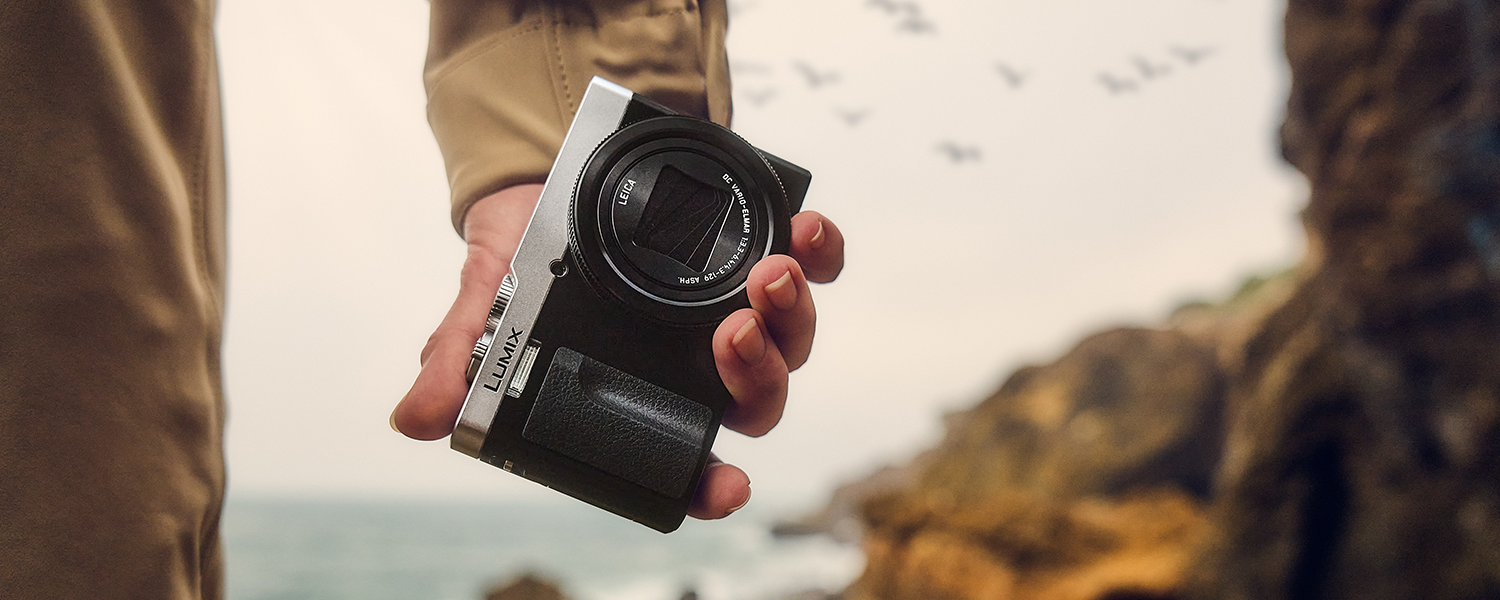 Person holds the LUMIX LX100MK2 camera at dusk with an old cityscape in the far background