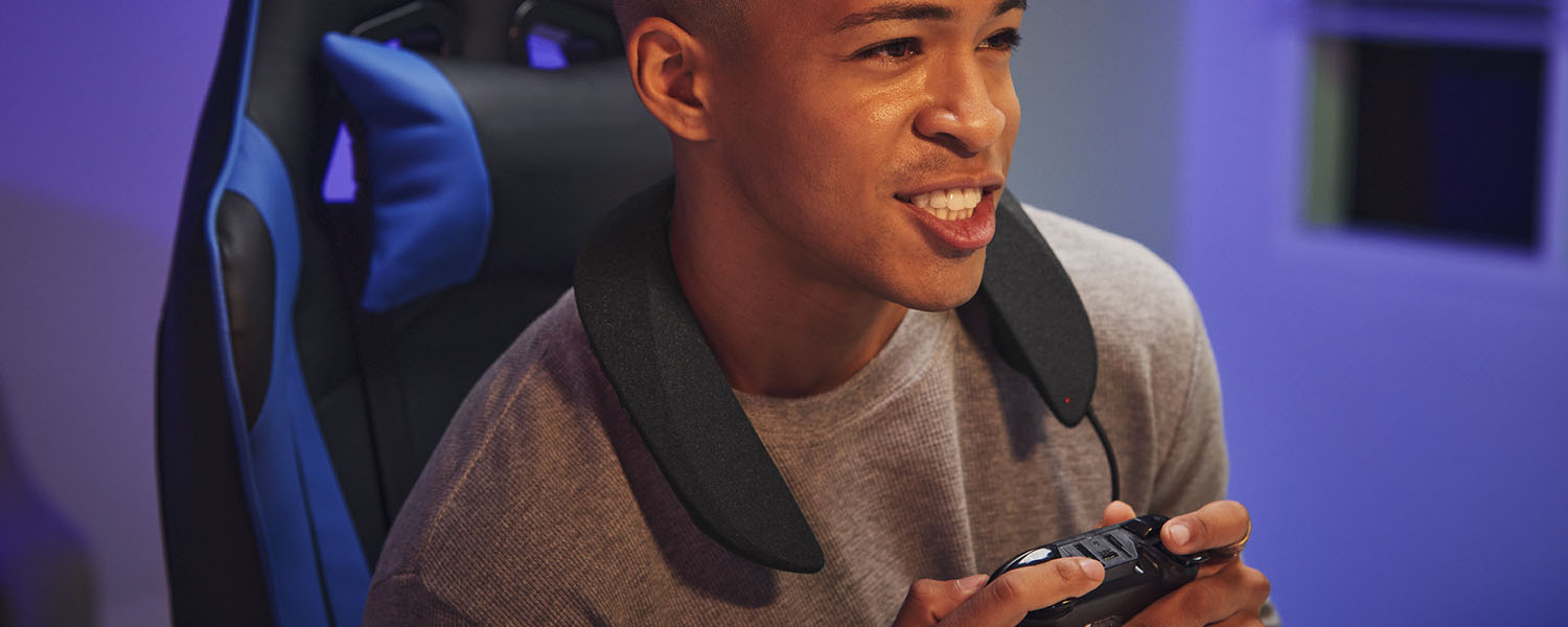 A young man is excitedly playing a video game on his computer wearing the Panasonic SoundSlayer wearable speaker system