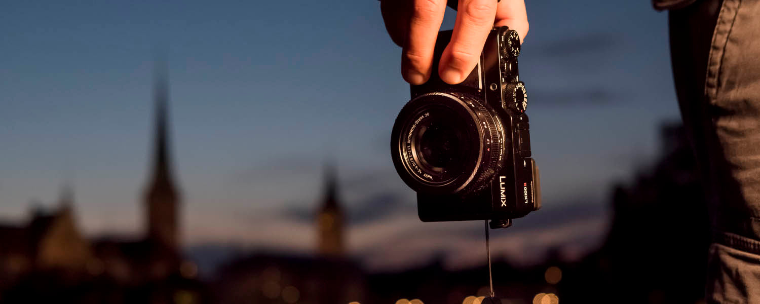 Person holds the LUMIX LX100MK2 camera at dusk with an old cityscape in the far background