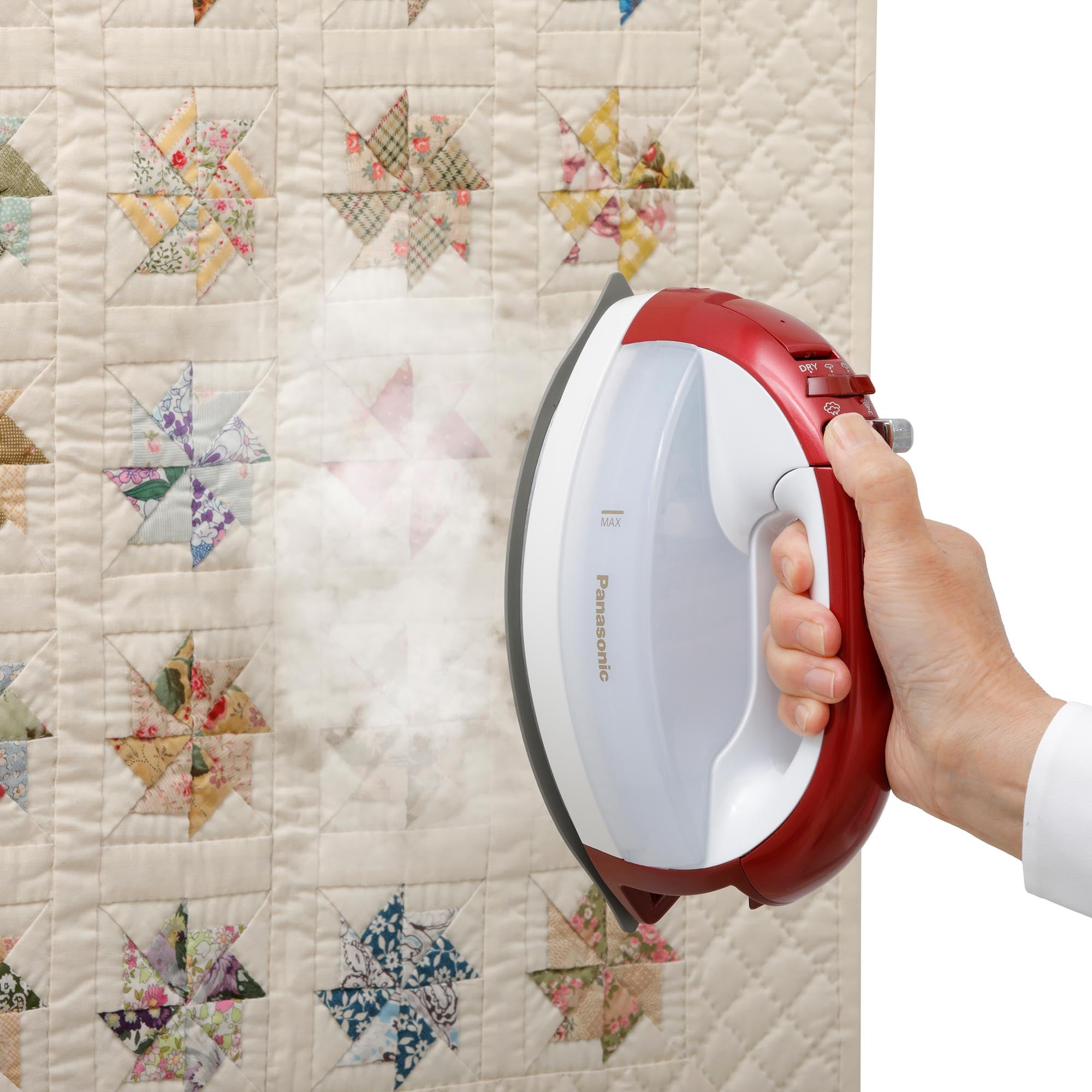 Person using Cordless Steam/Dry Iron, 1700W Wide Stainless Plate on a quilt with colorful patterns